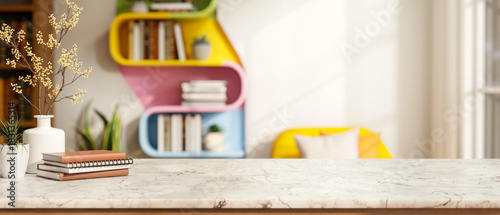 Fototapeta Naklejka Na Ścianę i Meble -  Books and flower vase on marble counter table across colorful wall bookshelf and sofa in living room