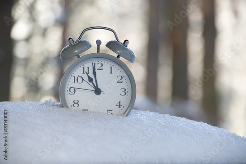 Alarm clock in snow, winter time concept, close up of clock face