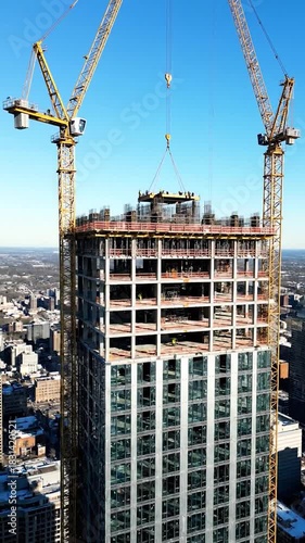 Skyscraper construction cranes lift materials to the unfinished upper floors, city view
