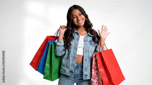 Smiling girl in denim with colorful shopping bags and a wave