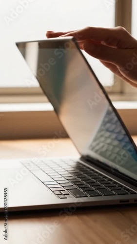 Hand hovers over a laptop keyboard, window light in background