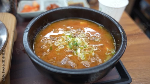 Spicy Korean Beef and Vegetable Soup (Yukgaejang) Served in Traditional Black Earthenware Bowl, Traditional Korean Stew (Jjigae) with Thinly Sliced Beef and Scallions on Wooden Table