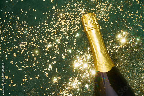 Champagne bottle on green surface with golden glitter