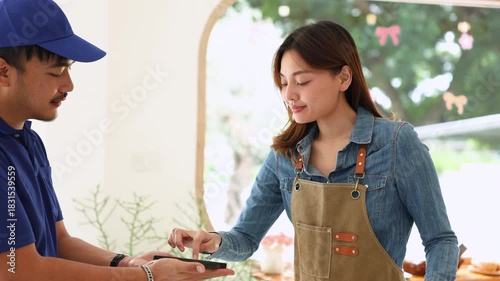 Courier and female small business entrepreneur verifying package via mobile device inside coffee shop, representing modern cashless payment, delivery service reliability, collaboration online orders