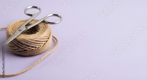 Ball of twine with scissors on a light purple background with copy space
