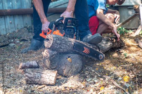 Grandfather teaching grandson how to cut wood with a chainsaw outdoors