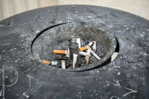Cigarette butts thrown in a dirty ashtray.