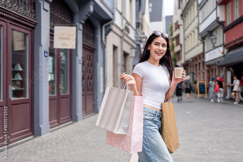 Mixed race woman hold shopping bags and drink while walk outdoors in city. 