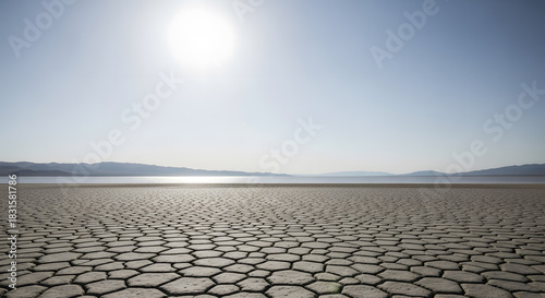 Cracked earth on a dry lake bed under a vast sky with distant mountains and sun
