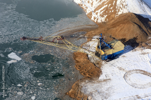 Aerial view of large dredge machine digging along icy shore