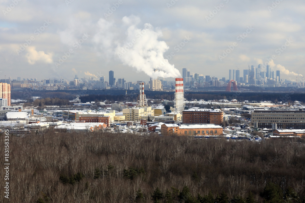 Fototapeta premium Industrial plant with smoking chimney and city skyline in background