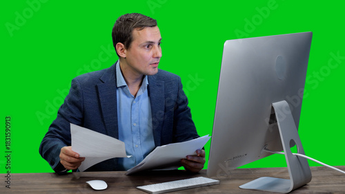 Young adult businessman holding contract in his hands and stares intently at the monitor screen against green background