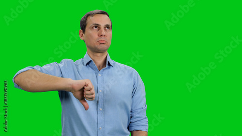 Thumb down sign gesture by young adult man expressing discontent disapproval dislike and disgust on green screen