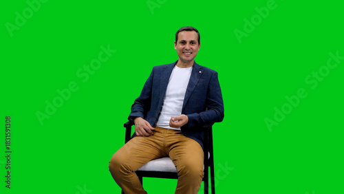 Young adult male vlogger sitting and talking in chair on green background