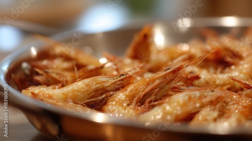 Close-up of a metal bowl filled with cooked shrimp. the shrimp are golden brown and appear to be seasoned with spices and herbs.