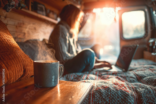 Digital nomad lifestyle captured in cozy vanlife setting with steaming cup of coffee, warm sunlight, and person working remotely on laptop, creating relaxed atmosphere