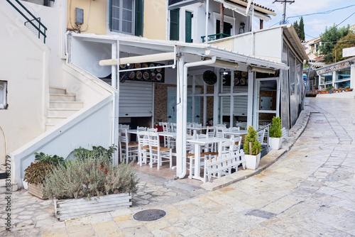 Fototapeta Naklejka Na Ścianę i Meble -  Traditional Greek taverna with white chairs on a cobblestone street