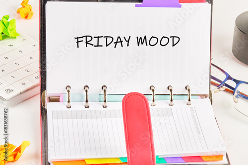 An open personal organizer displays the words FRIDAY MOOD. A calculator, glasses, and crumpled paper sit nearby on a white desk, hinting at a busy weeks end