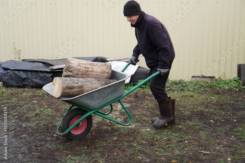 Fotografia Senior man doing yard work, pushing a wheelbarrow loaded with firewood logs