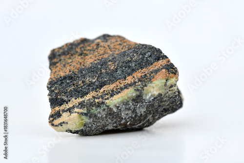 Photography Macro shot of a dark, striated rock specimen with black and orange/brown layers on a reflective white surface, perfect for geology and science concepts