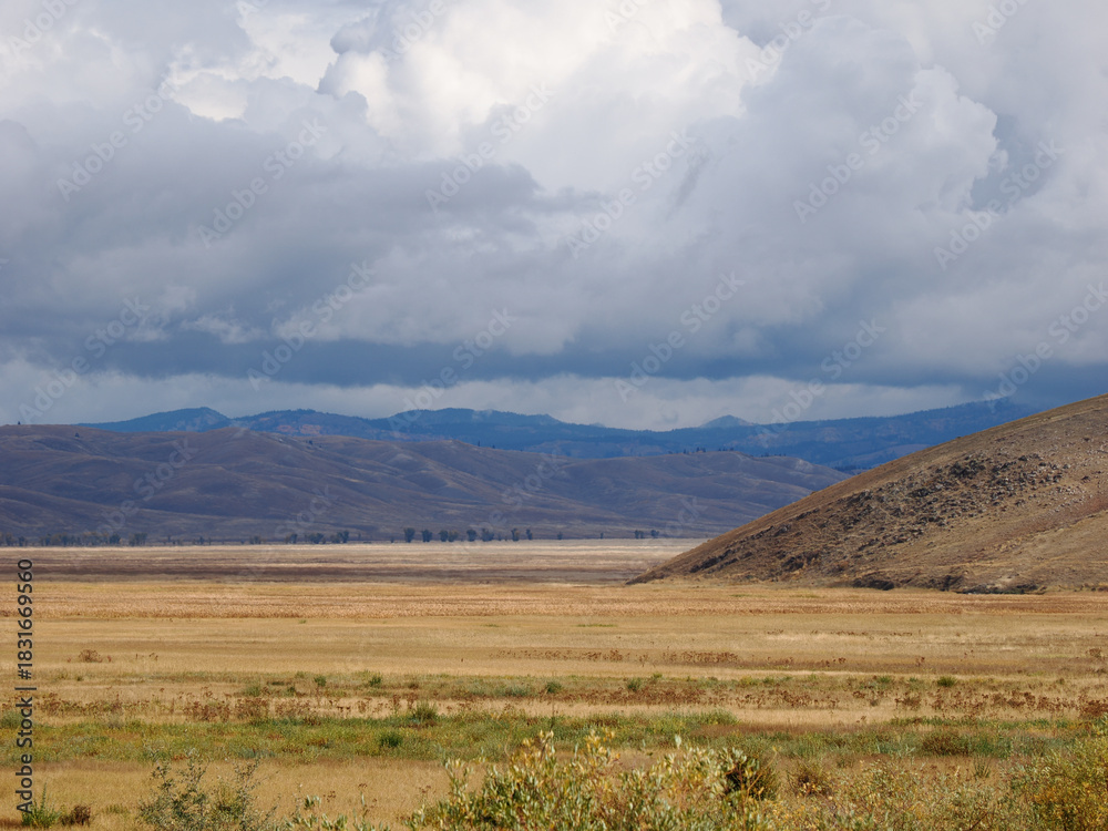 Obraz premium Expansive, arid valley and hills landscape under heavy, dramatic storm clouds