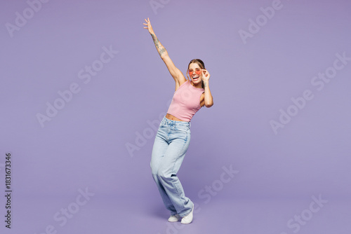 Full body young happy cheerful fun cool woman she wear pink tank top casual clothes sunglasses dance raise up hands isolated on plain pastel light purple background studio portrait. Lifestyle concept.