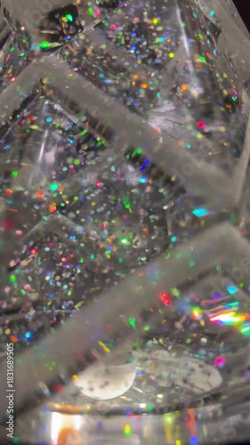 Close-up view of a snow globe as bright, colorful sprinkle-like particles float and swirl around an interior scene, creating a playful and festive visual with shallow depth of field.