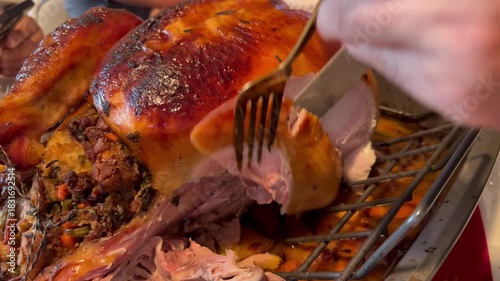 Close-up video of hands carefully carving tender breast meat from a golden brown oven-roasted turkey, with a family holiday meal taking place in the background during Thanksgiving or Christmas dinner.