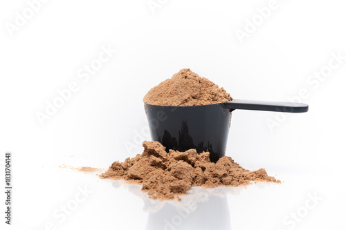 Horizontal image of chocolate whey protein in and around  a scoop. White background with a reflective surface.