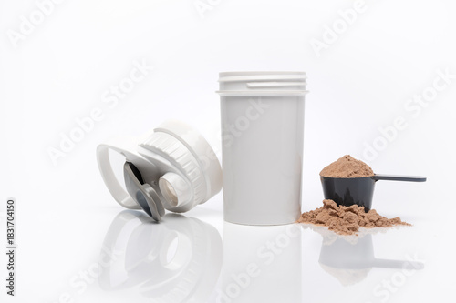 Horizontal image of a shaker cup with whey protein in a scoop next to it. White background with a reflective surface.