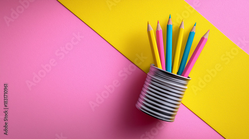 Colorful pencils stand in a tin can on vibrant pink and yellow background. Bright setting enhances visual appeal in creative spaces. Concept of art supplies, design, stationery