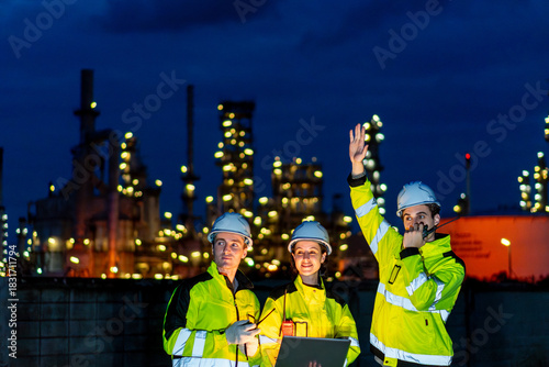 Petrochemical industry night engineer teamwork working on laptop Team of Petroleum in Glowing Workwear Collaborating oil refinery plant construction site at night