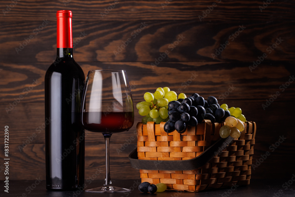 Naklejka premium Red wine bottle with a glass and basket of fresh grapes