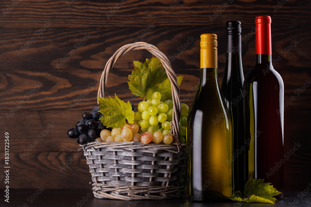 Naklejka premium Red and white wine bottles with a glass and basket of fresh grapes
