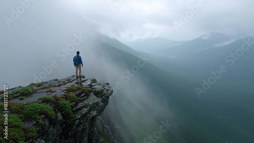 Lone hiker stands on misty mountain cliff overlooking foggy valley