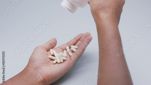 White capsules or pills being poured from a plastic bottle into a hand against a light gray background. Concept of medicine, healthcare, supplements, and pharmaceutical treatment.
