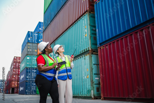 Workers in safety gear communicate status updates, confirming operational tasks and reviewing delivery timelines during an on-site meeting in a container yard.