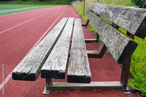 Konzept: Trainer, Zuschauer, Auswechselspieler: Eine alte Holzbank in einem Fußballstadion steht am Rand des Spielfeldes neben einer Tartan Laufbahn für Leichtathletik