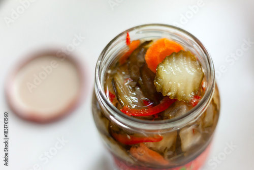 An open jar of cucumbers, carrots and peppers in brine