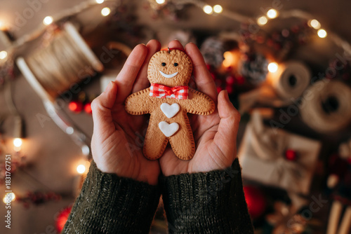 Hand holding a cheerfully decorated gingerbread man cookie, with a colorful, warm Christmas backdrop