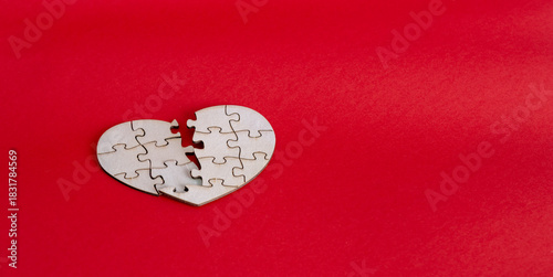 Broken wooden heart puzzle symbolizing heartbreak separation loss on red background