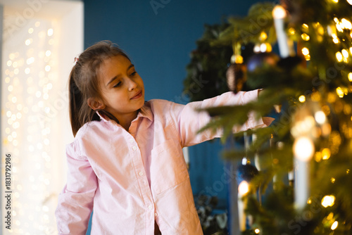 Young girl decorates Christmas tree at home with joy during festive season in early December