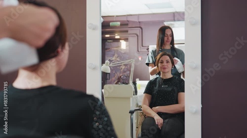 stylist finishes client protection gear, female customer receives cape placement near mirror, calm professional prepares client with cape adjustment during salon reflection and lighting