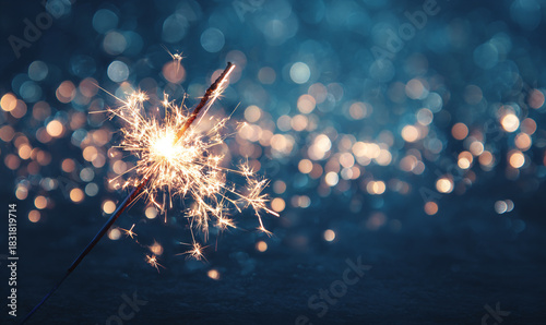 A sparkler burning brightly against a blurred background of bokeh lights glow