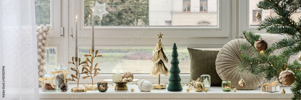 Obraz premium Christmas window sill with candles, trees and ornaments in gold and green. Cozy and natural festive arrangement with soft daylight.