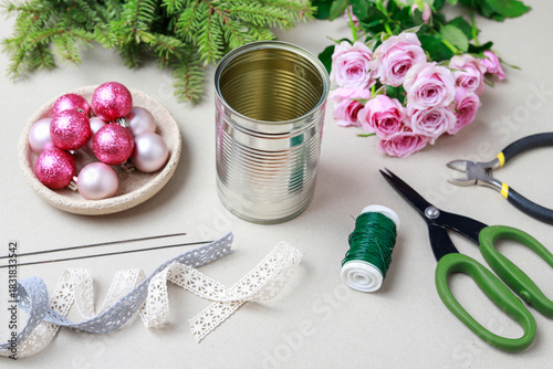 Florist at work: woman shows how to make modern Christmas decoration with fir, roses, pink baubles and decorative stars. The base is classic can. Step by step, complete tutorial.