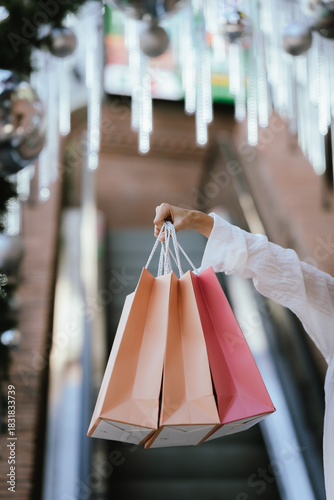 A smiling woman carries multiple shopping bags while walking outdoors near festive Christmas decorations, creating a cheerful holiday shopping vibe.