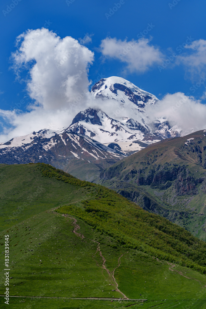 Fototapeta premium Mount Kazbek towering above green hillside hiking trail