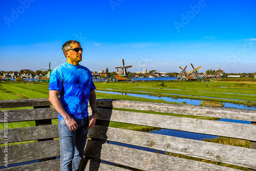 Side profile of a traveler wearing sunglasses and blue shirt admiring the Dutch countryside landscape.