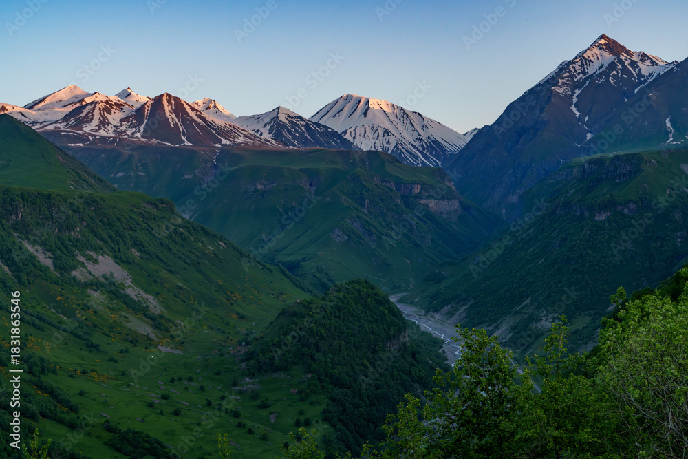 Fototapeta premium Sunset light on snowy Caucasus peaks above green river valley